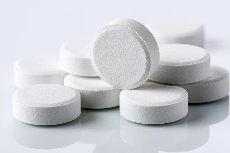 Round white pharmaceutical tablets scattered on a reflective white surface