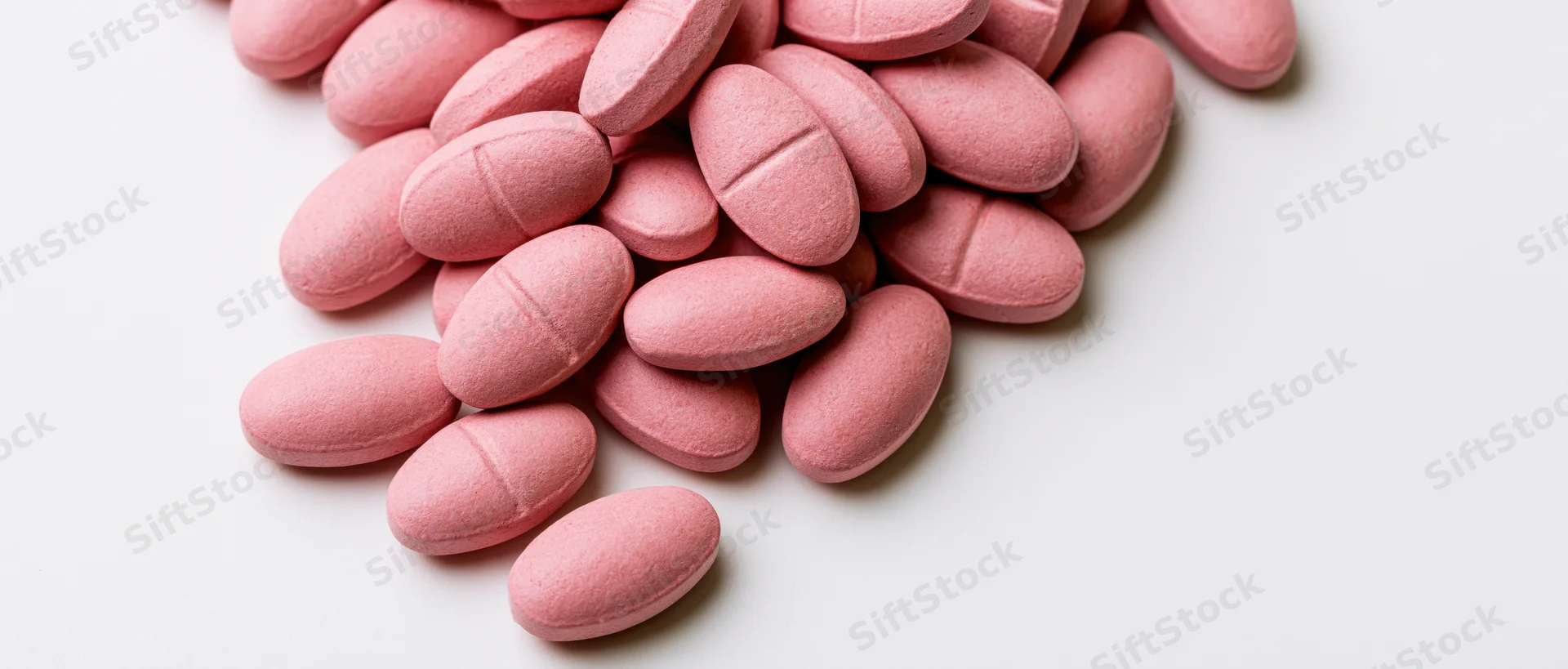 Oval pink scored tablets scattered on a clean white surface