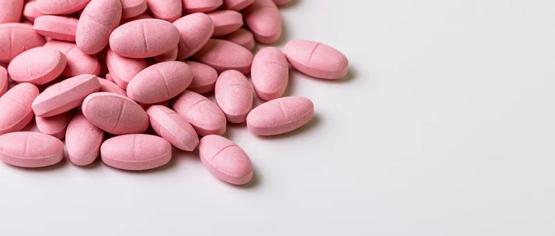 Pink oval scored tablets scattered on a white surface