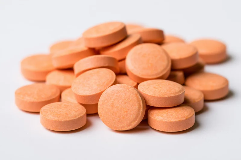 Pile of small round orange vitamin tablets scattered on white surface