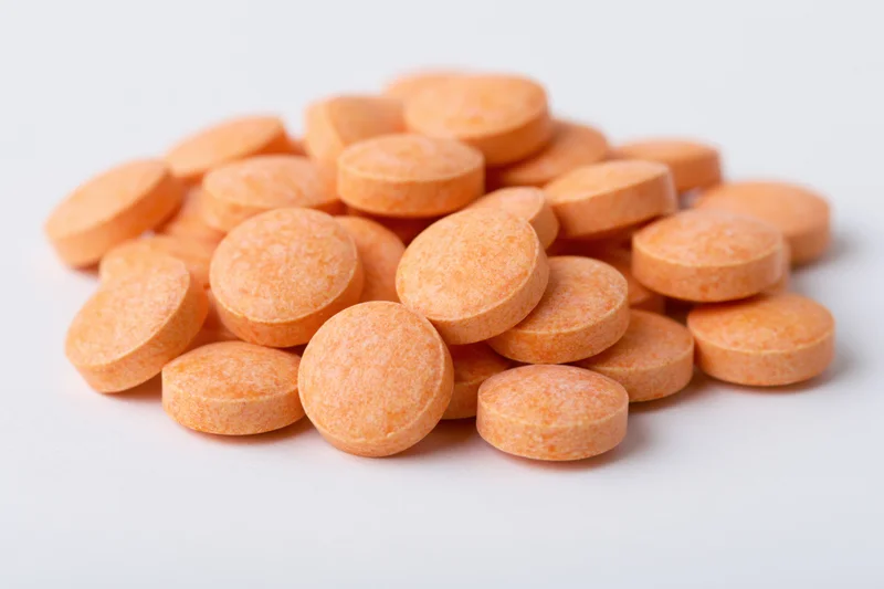 Loose pile of small round orange vitamin tablets scattered on white surface