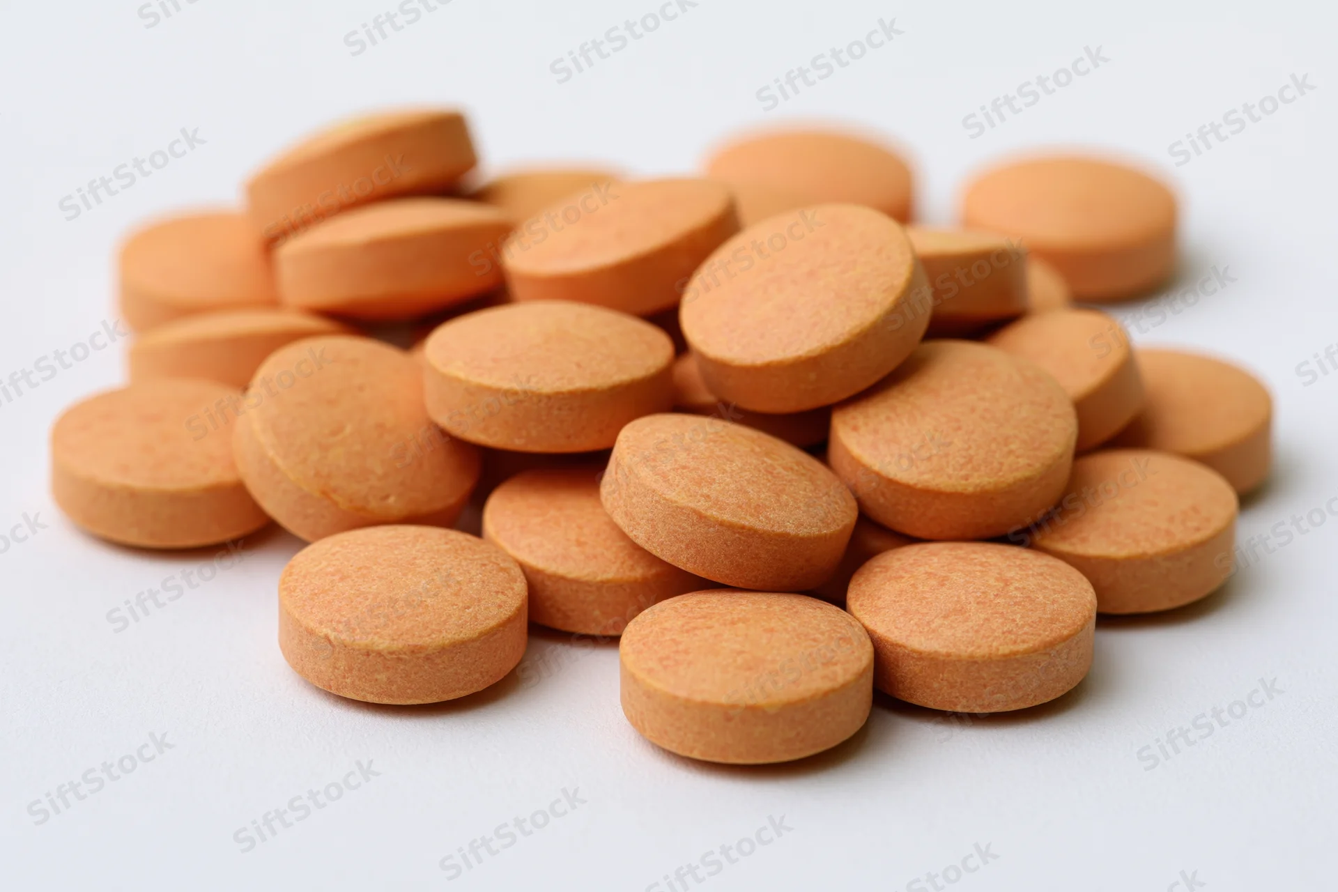 Loose pile of small round orange vitamin tablets scattered on white surface