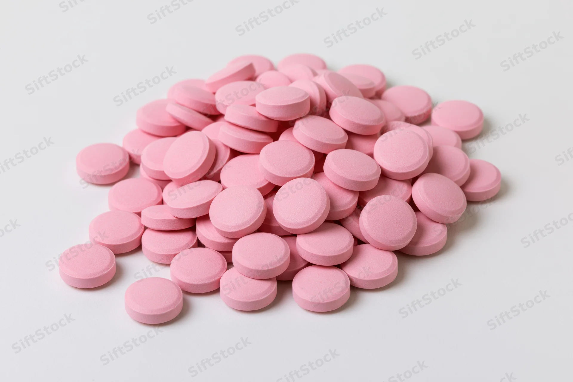 Pile of small round pink coated tablets scattered on white surface