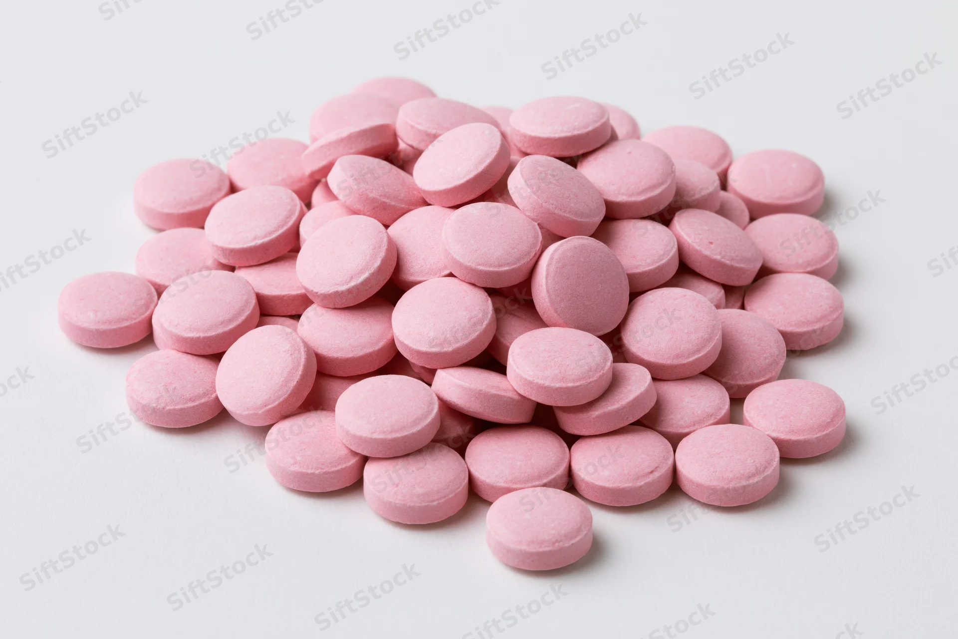 Pile of small round pink coated tablets scattered on white surface