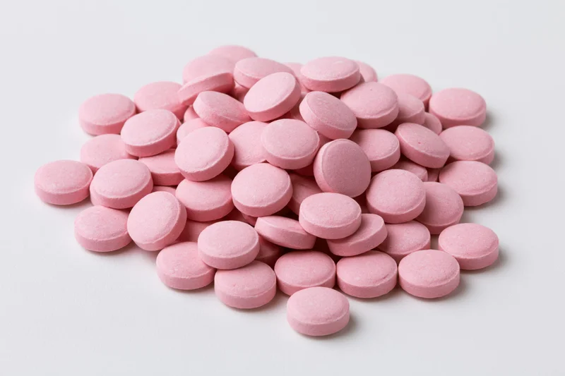 Pile of small round pink coated tablets scattered on white surface