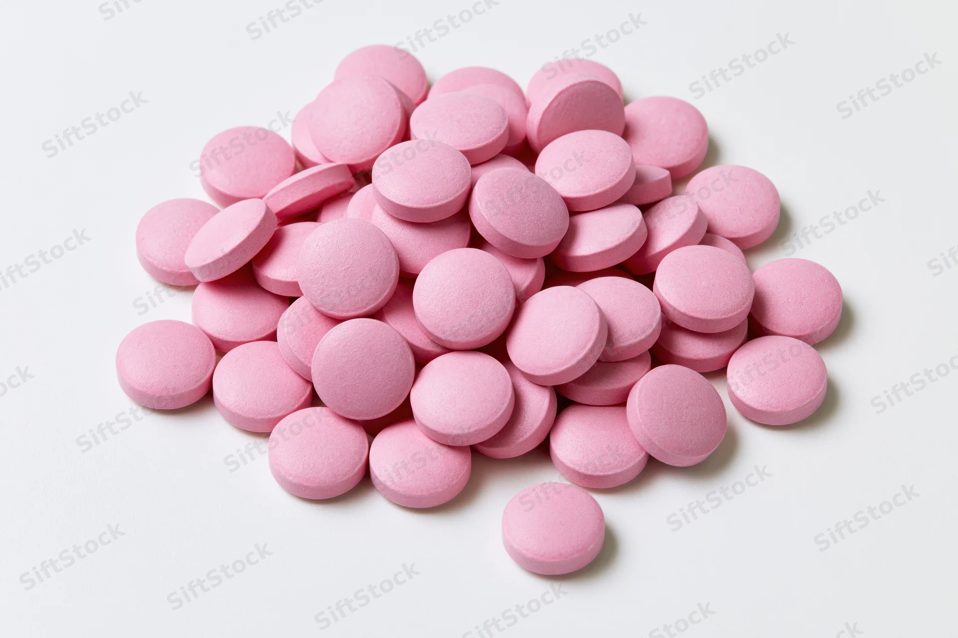 Pile of small round pink coated tablets scattered on white surface