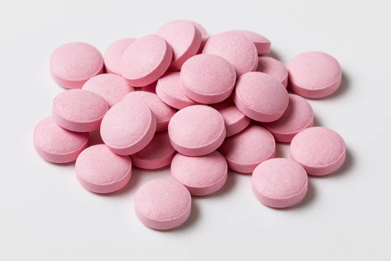 Pile of small round pink coated tablets scattered on white surface