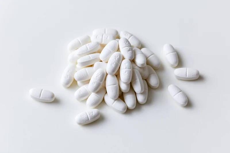 White oval scored tablets scattered in a loose pile on a plain white surface