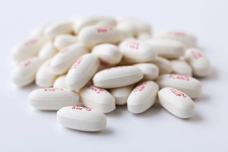 White oval caplet tablets with red imprints piled on a plain white surface