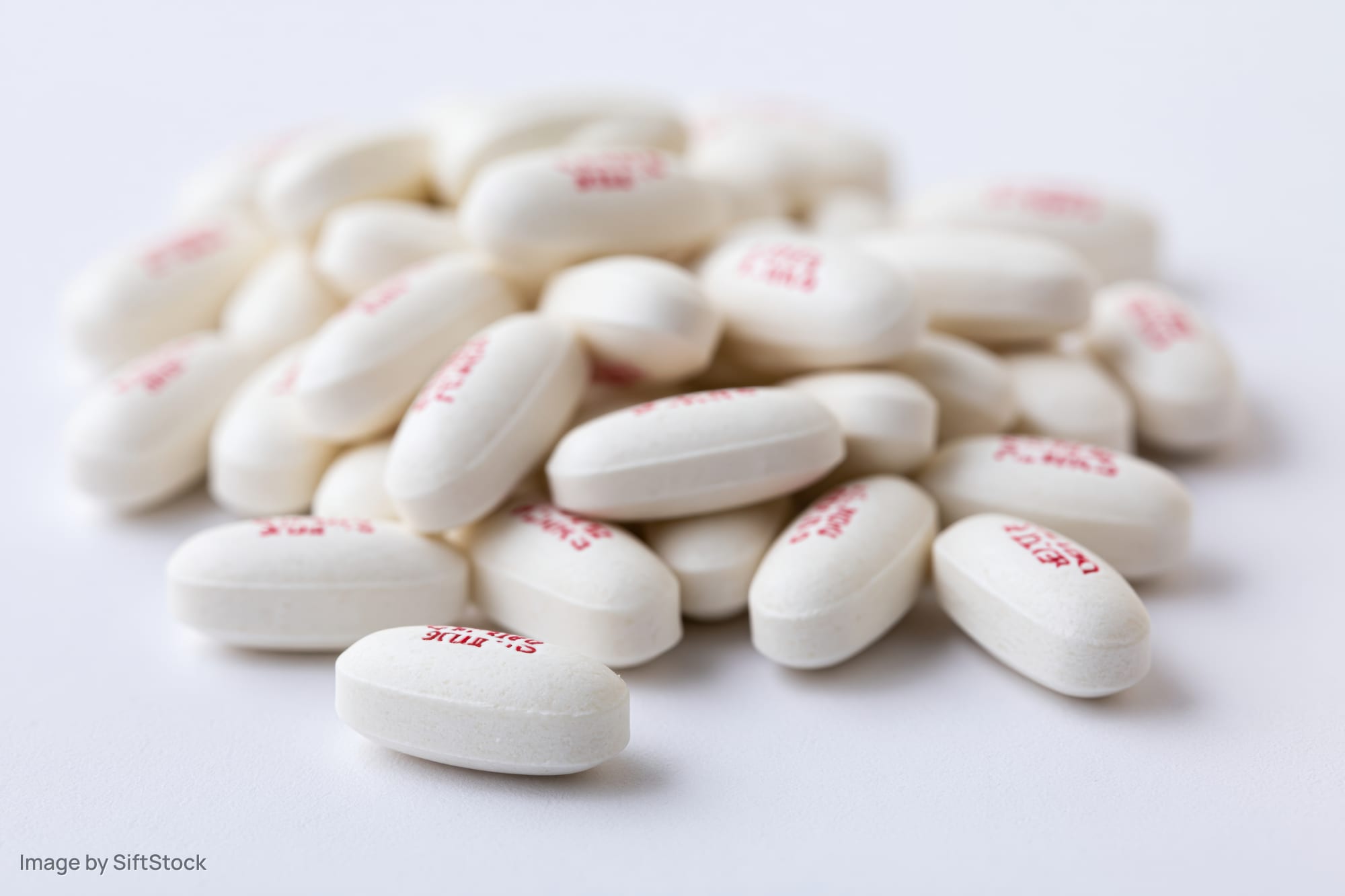 White oval caplet tablets with red imprints piled on a plain white surface