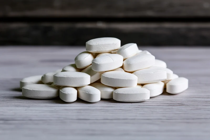A pile of white oval tablets on a pale grey wooden surface