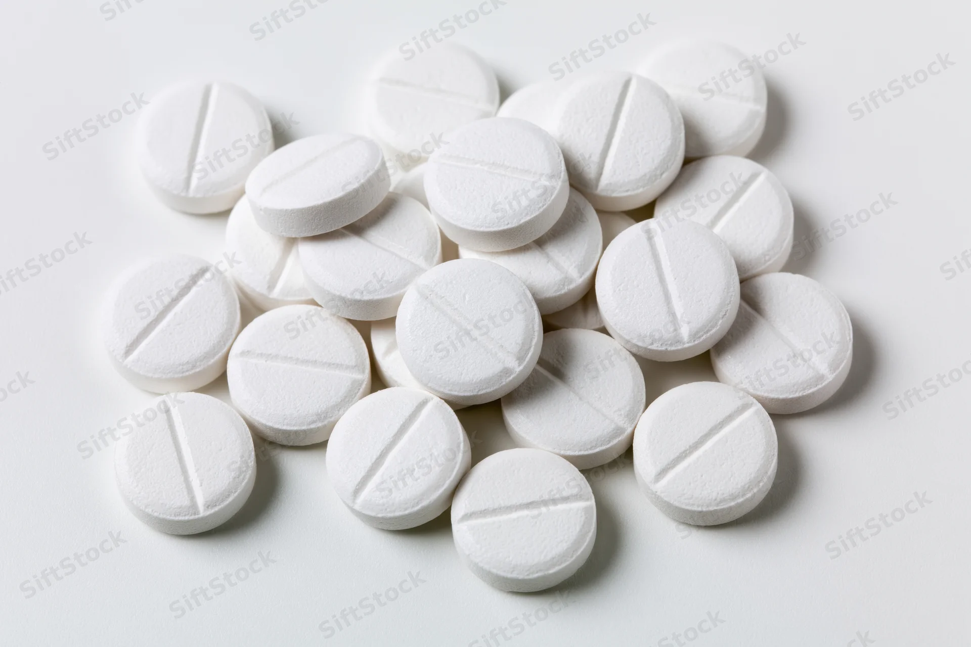 Scattered white pharmaceutical tablets on a plain white surface