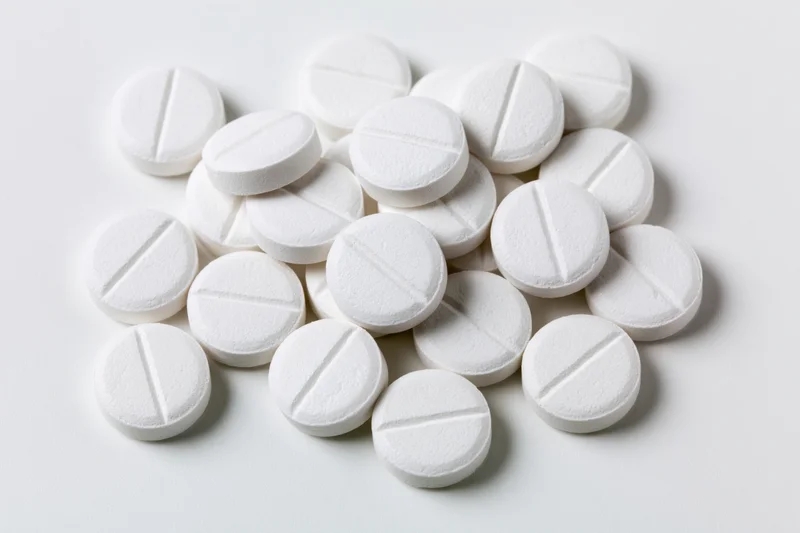 Scattered white pharmaceutical tablets on a plain white surface