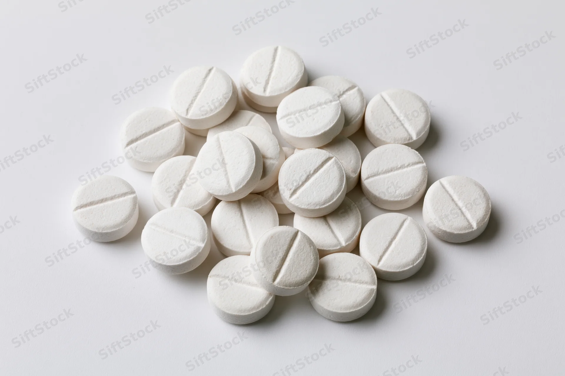 Scattered white round pharmaceutical tablets on a plain white surface