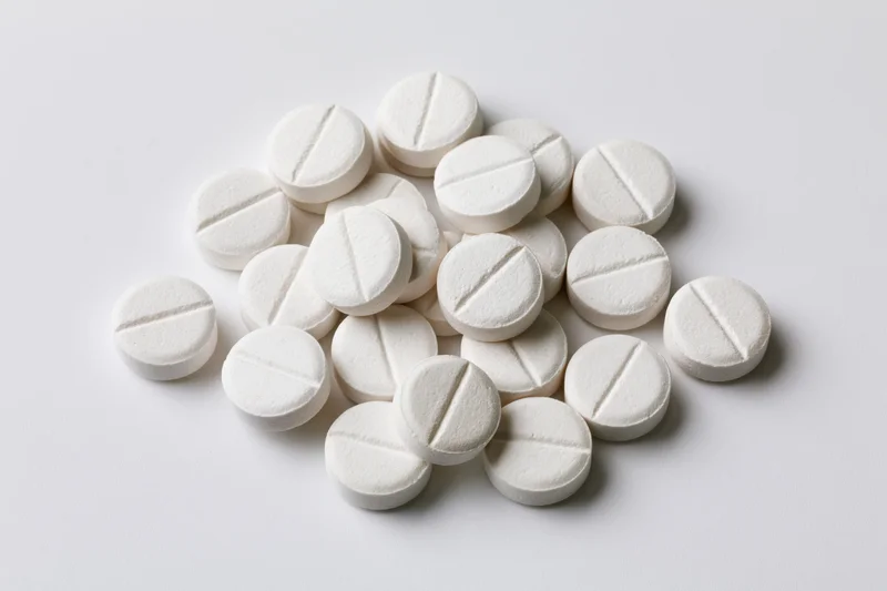 Scattered white round pharmaceutical tablets on a plain white surface