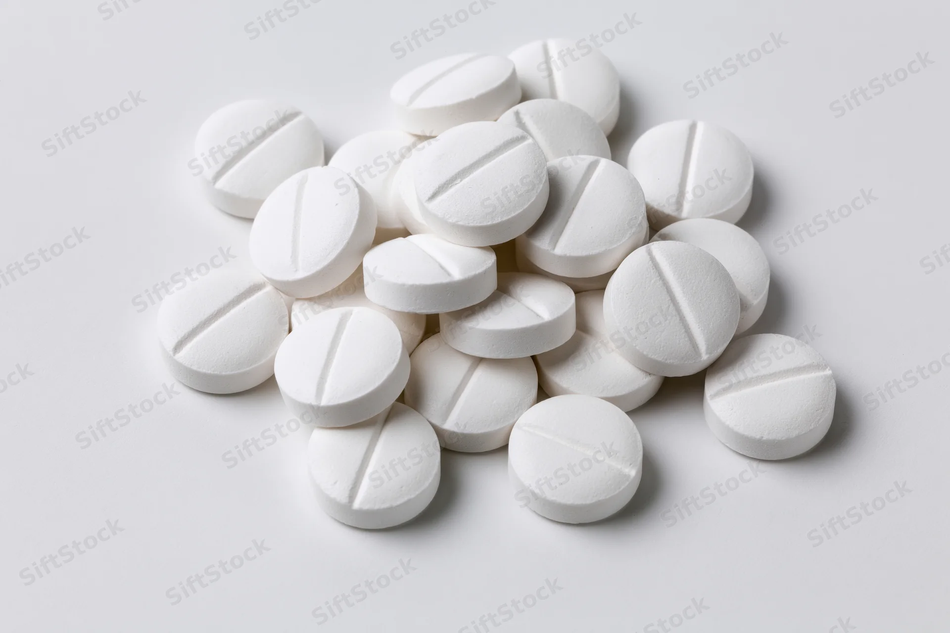 Scattered white pharmaceutical tablets on a plain white surface