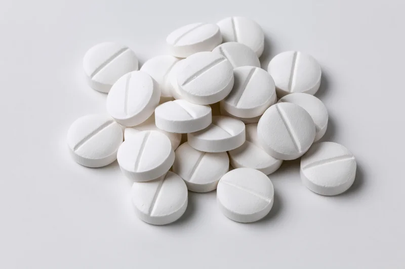 Scattered white pharmaceutical tablets on a plain white surface