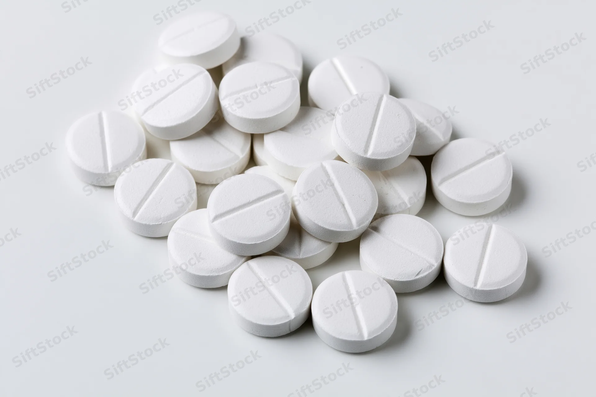 Scattered white pharmaceutical tablets on a plain white surface