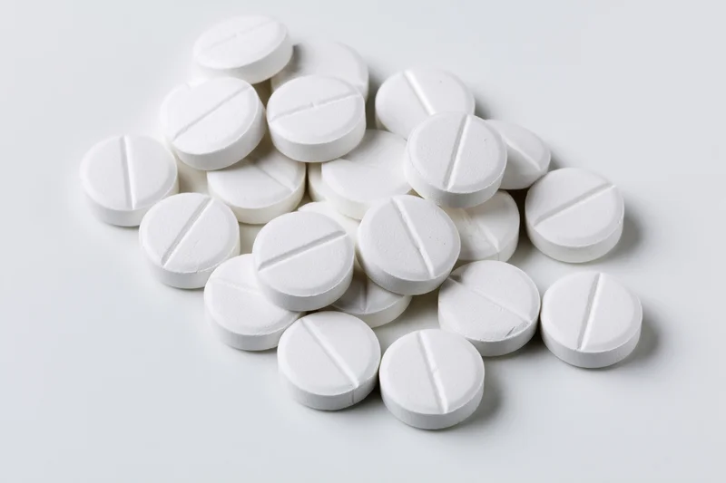 Scattered white pharmaceutical tablets on a plain white surface