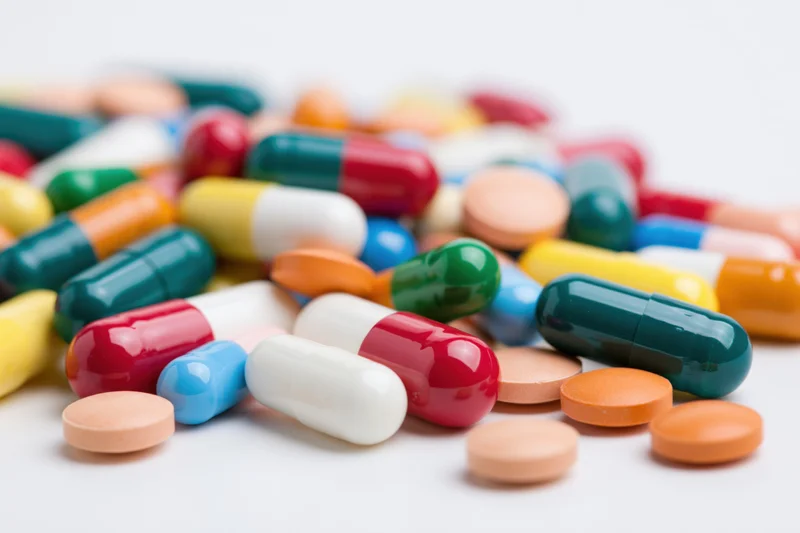 Scattered pile of colorful pharmaceutical capsules and tablets on white background