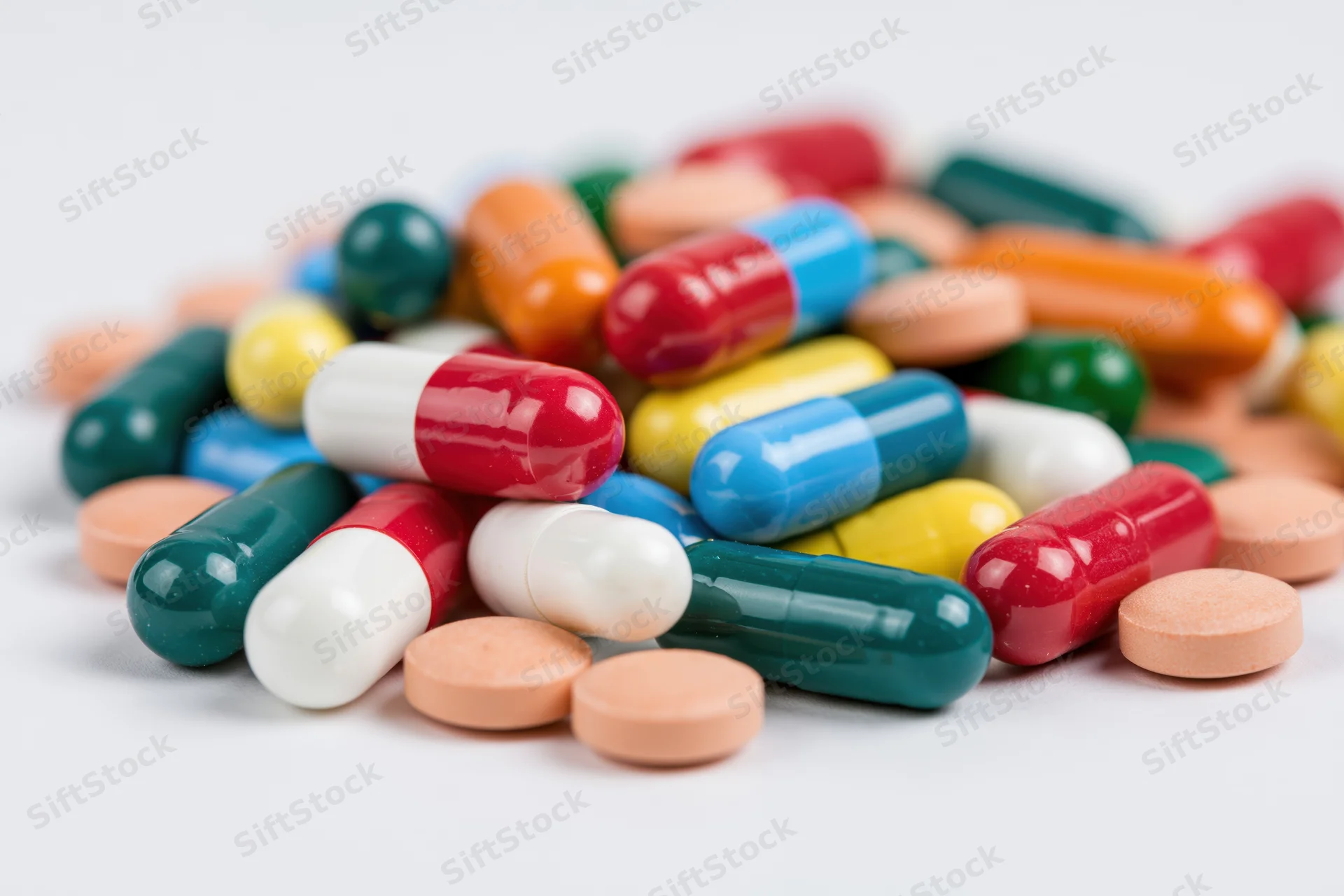 Scattered pile of colorful pharmaceutical capsules and tablets on white surface