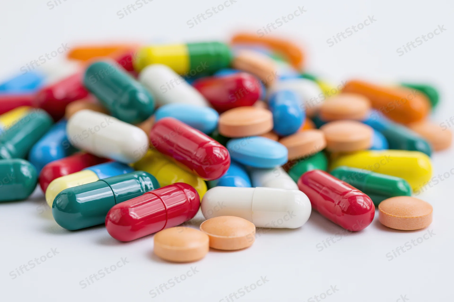 Scattered pile of colorful pharmaceutical capsules and tablets on white surface
