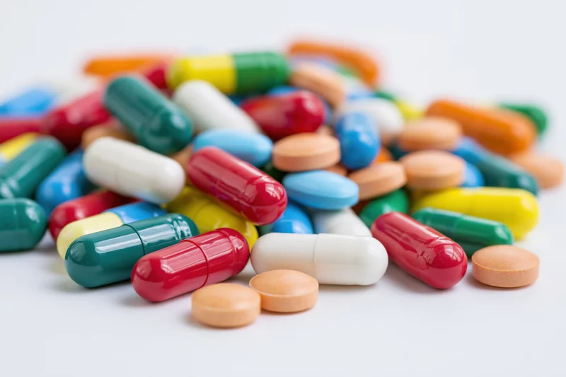 Scattered pile of colorful pharmaceutical capsules and tablets on white surface