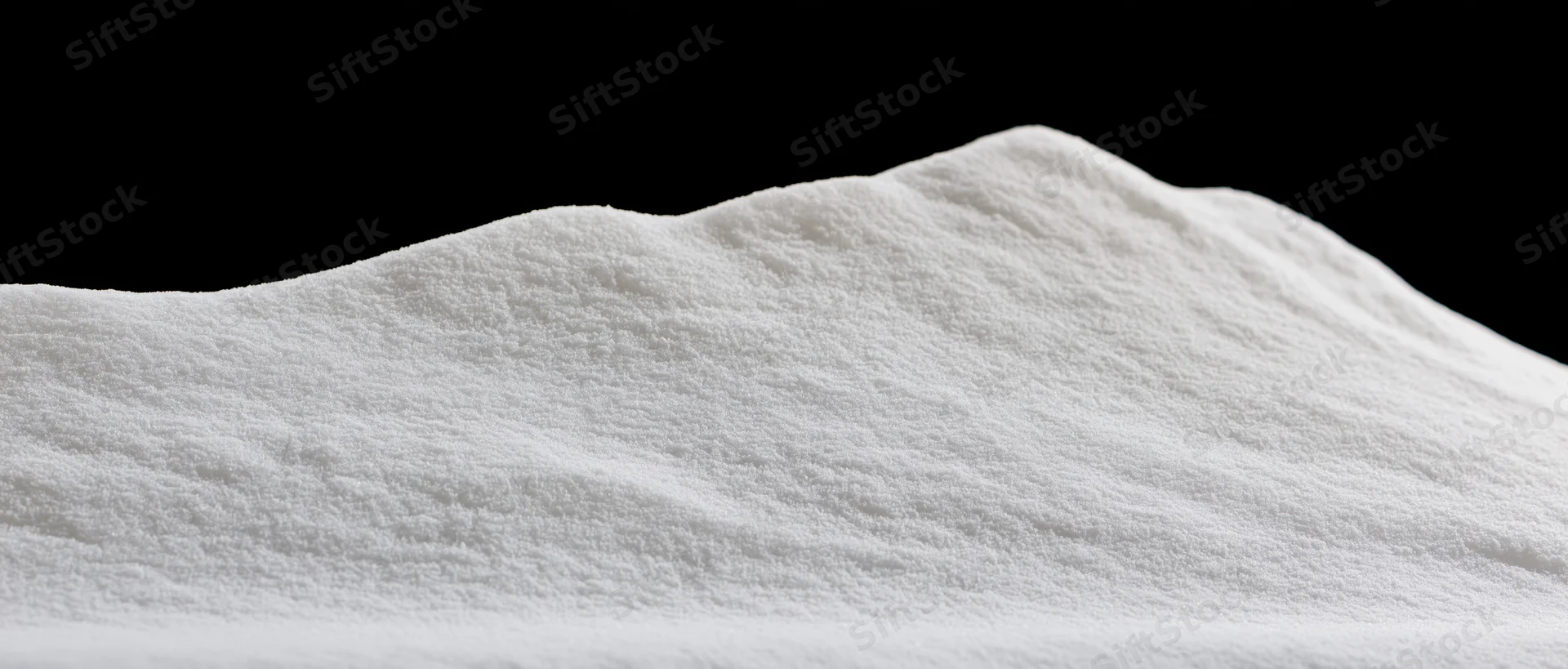 Closeup of a soft white powder pile with undulating ridges against black background