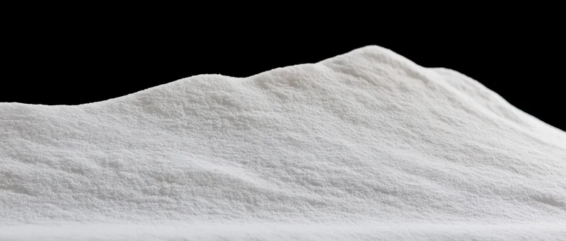 Closeup of a soft white powder pile with undulating ridges against black background