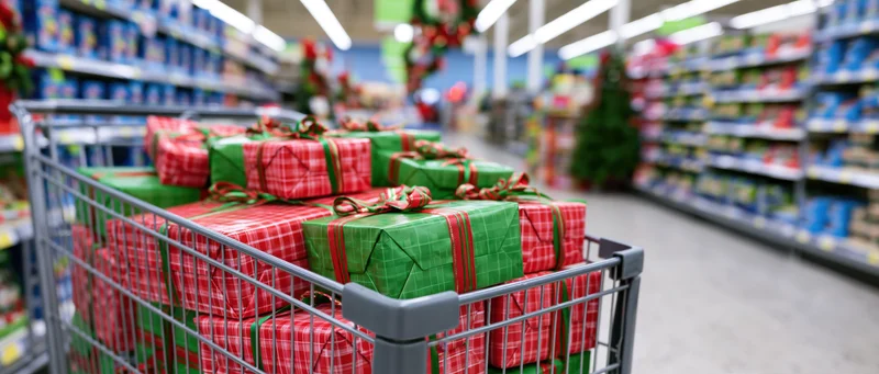 Metal shopping cart overflowing with wrapped christmas gifts in supermarket aisle