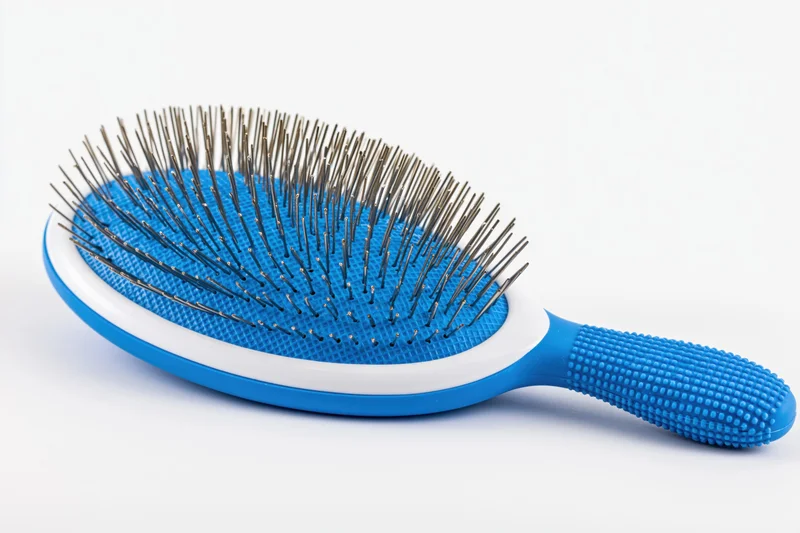 Blue pet slicker brush with textured rubber handle and metal bristles on white background