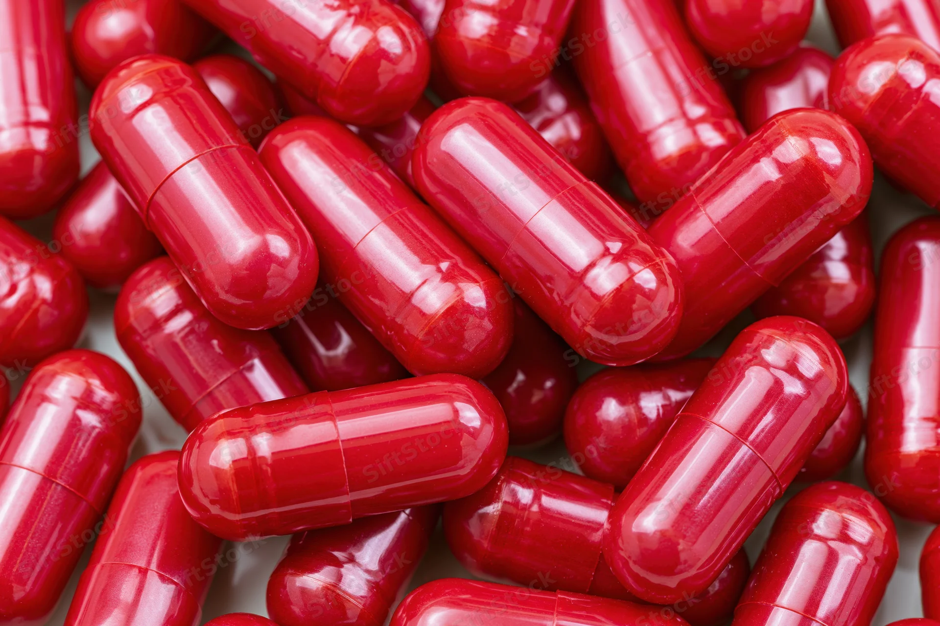 Bright red gelatin capsules scattered in a pile on a white surface
