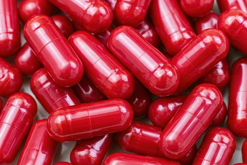 Bright red gelatin capsules scattered in a pile on a white surface