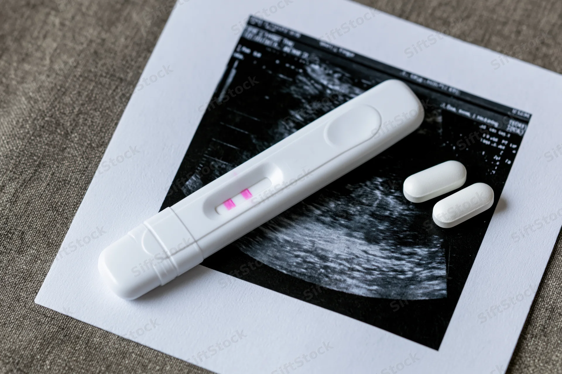 Positive pregnancy test with two pink lines resting on ultrasound scan print on textured surface