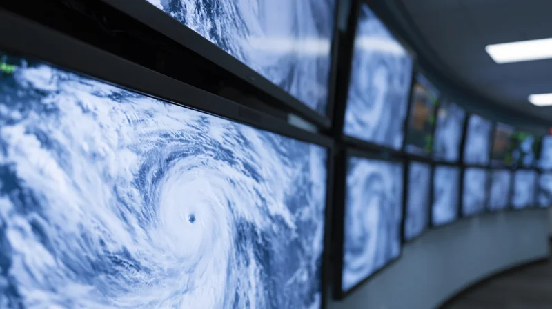 Satellite view of hurricane displayed on curved wall of monitors in control room