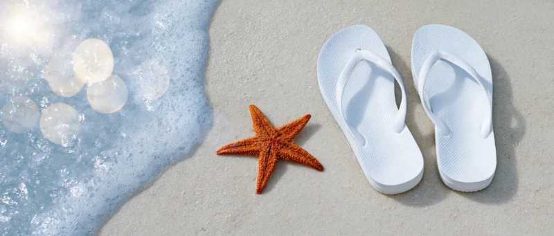 Starfish on wet sand beside white flipflops near ocean foam