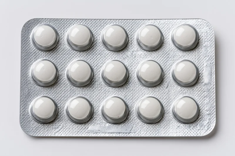 Fifteen round white pills in a silver aluminum blister pack on a plain white surface