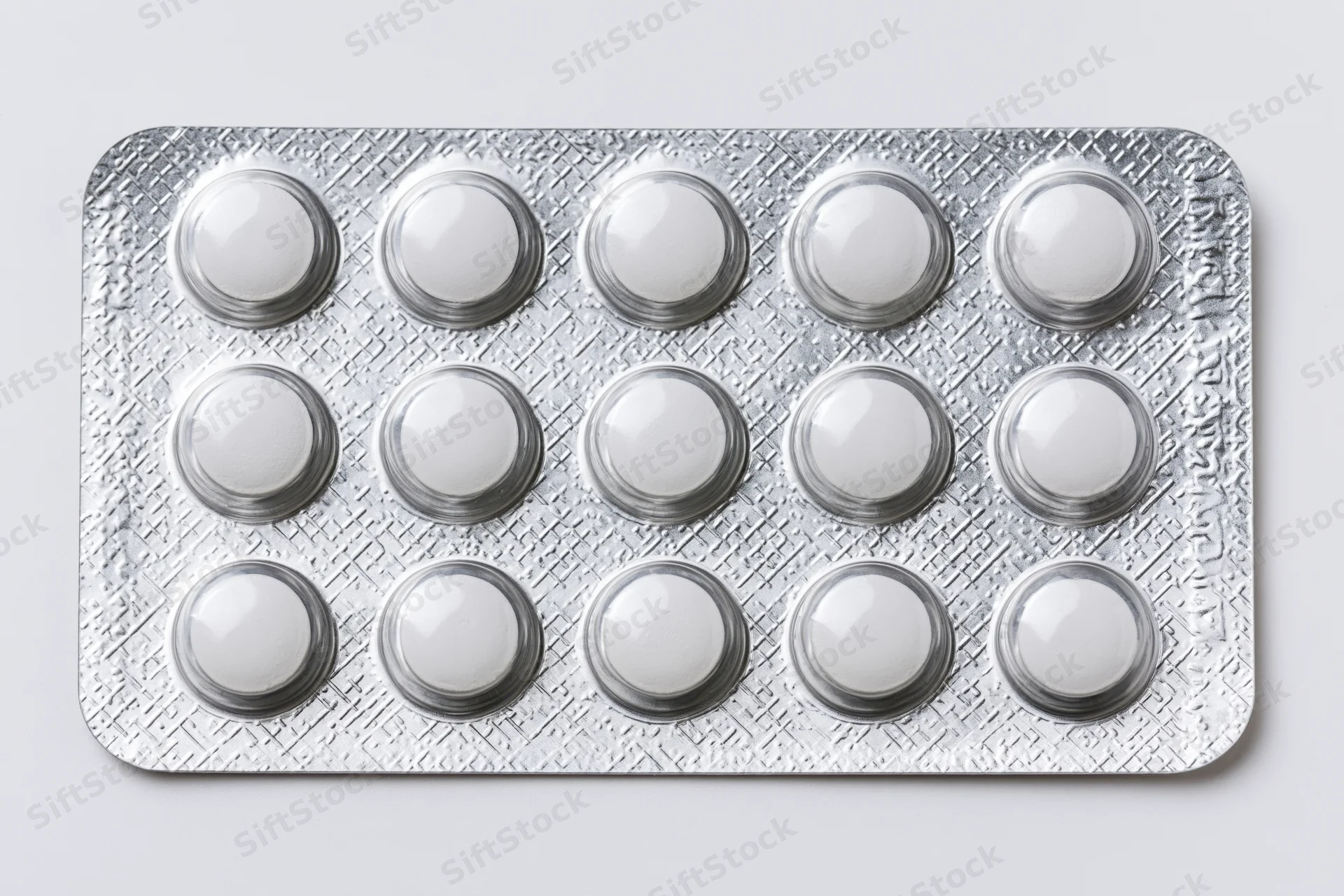 Silver aluminum blister pack with fifteen round white tablets on plain background
