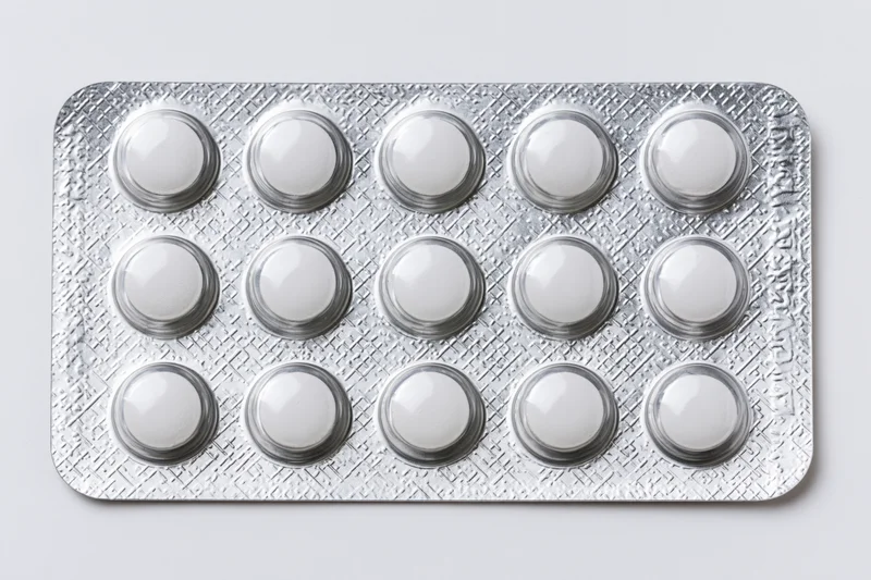 Silver aluminum blister pack with fifteen round white tablets on plain background