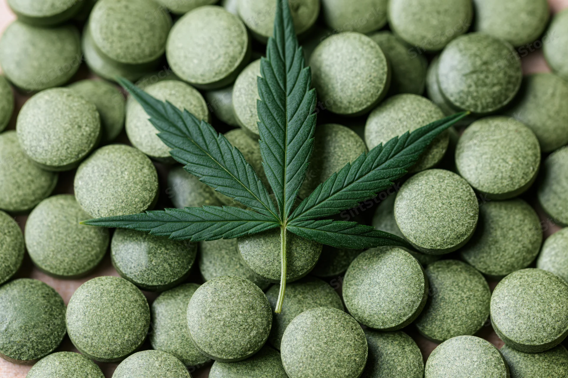 Cannabis leaf resting on a pile of green tablets