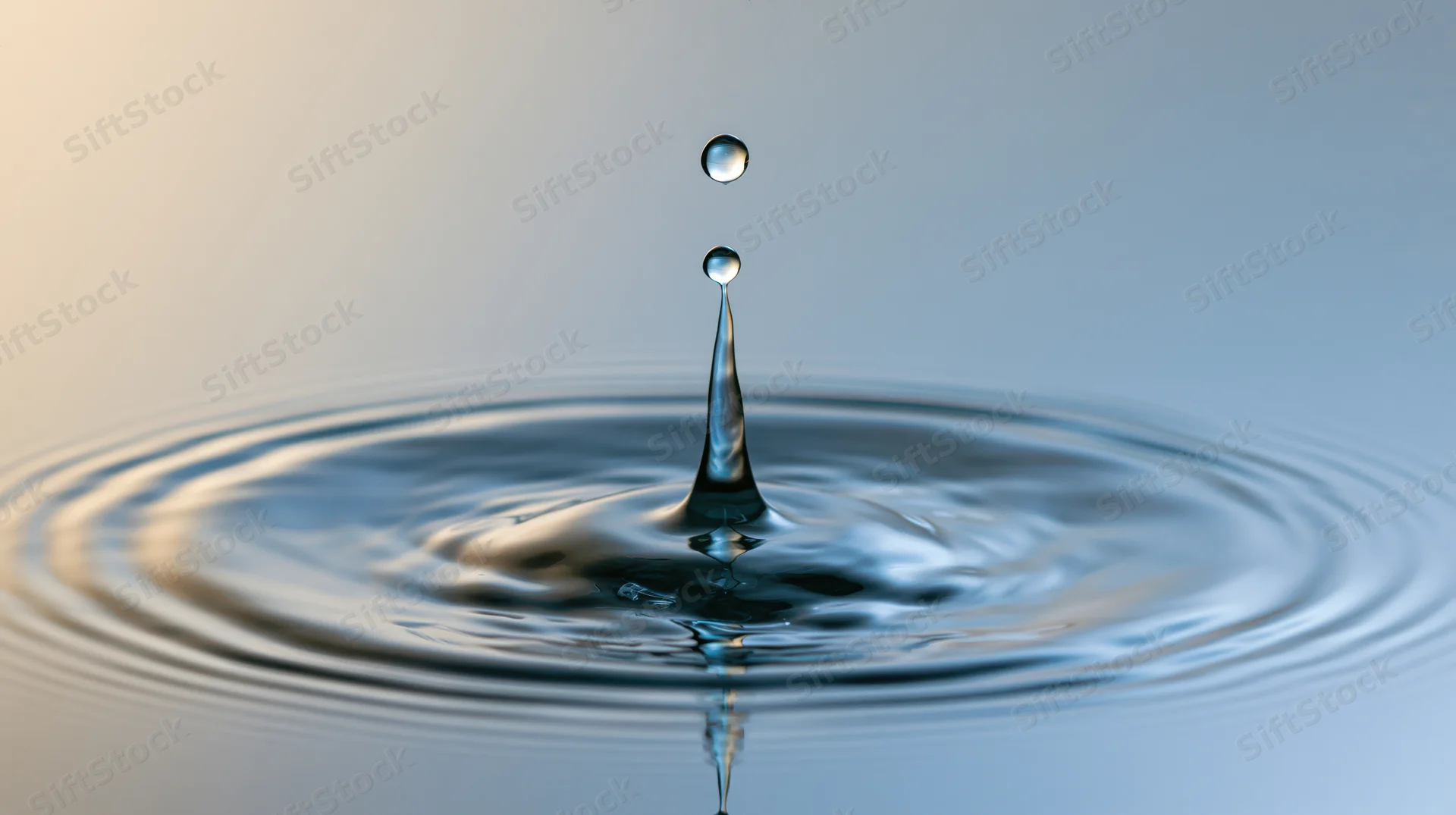 Water droplet mid-collision with calm surface creating ripples and reflection
