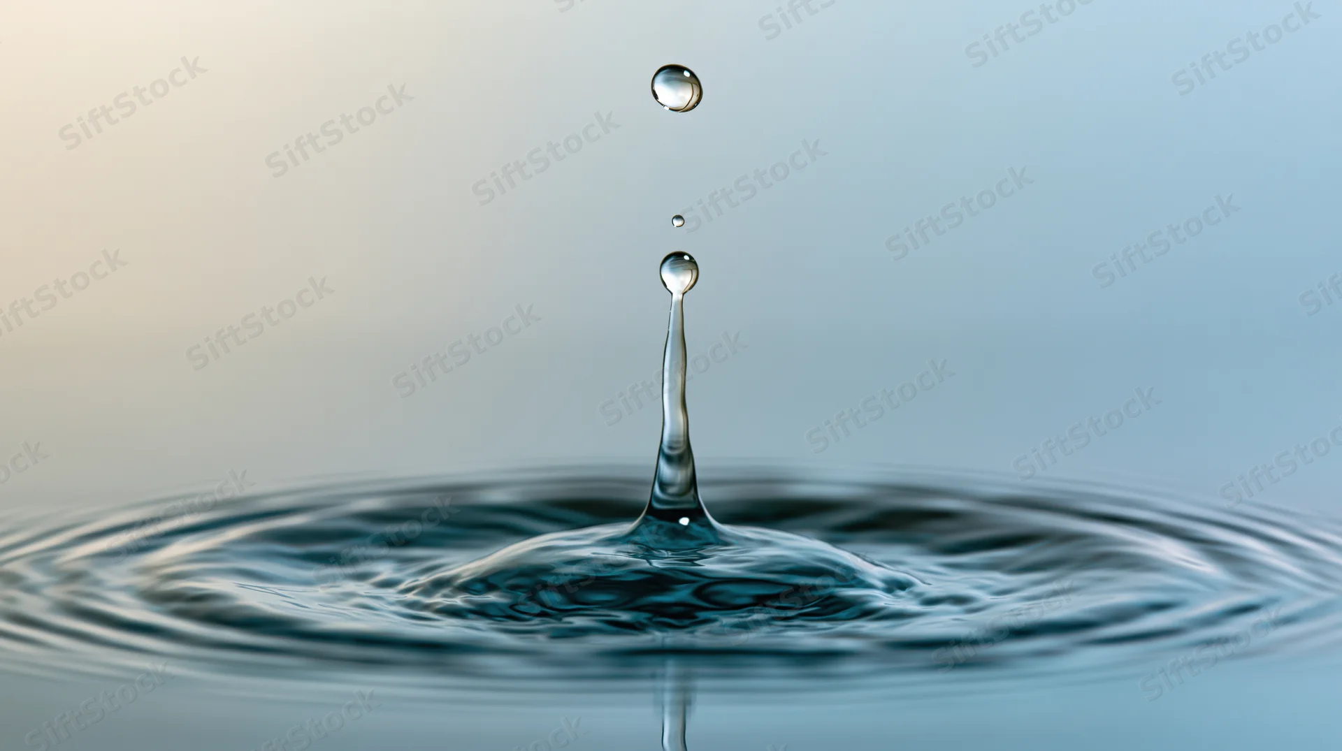 Water droplet mid-collision with calm surface creating splash and ripples