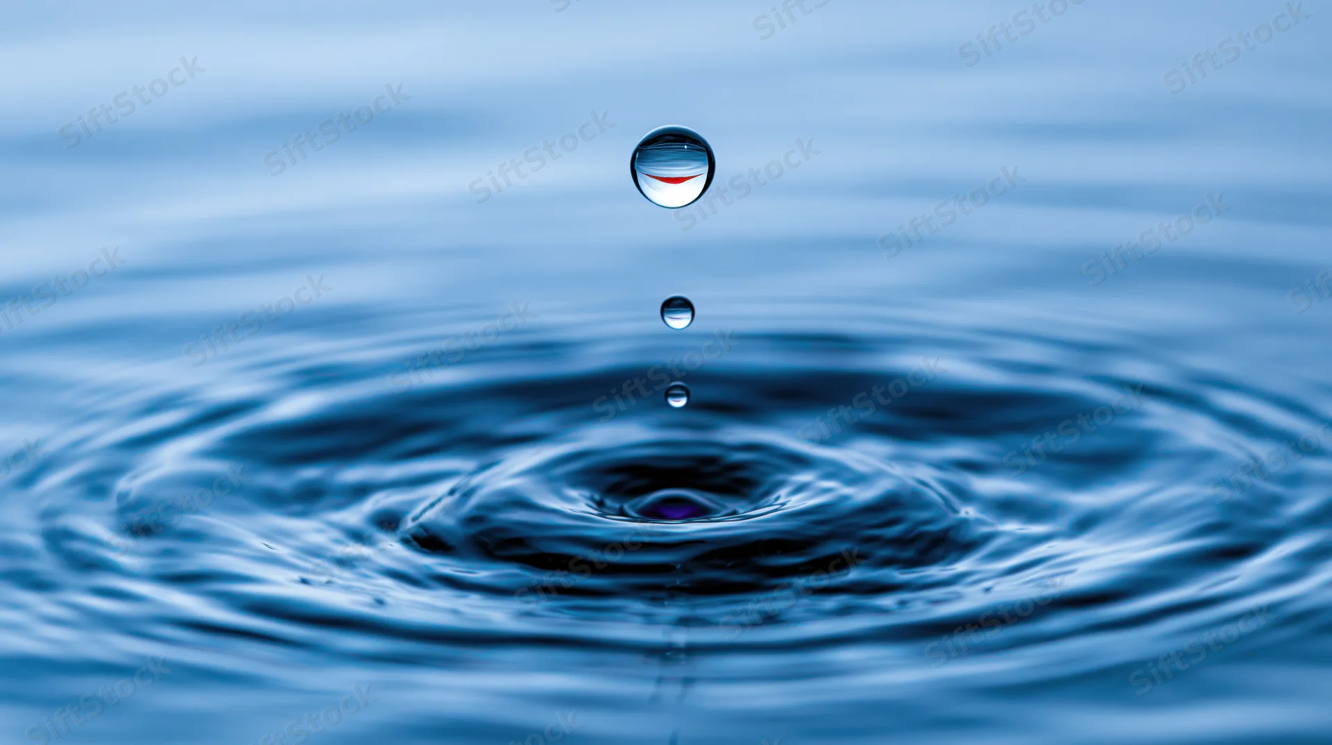 Water droplet suspended above rippling surface creating concentric waves