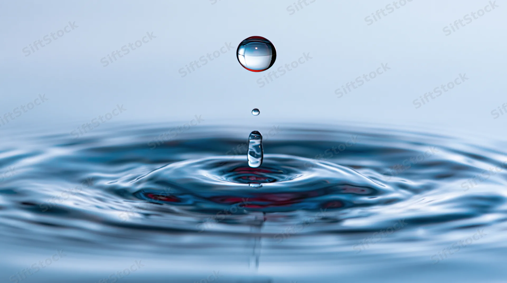 Water droplet suspended above rippling surface in mid-splash