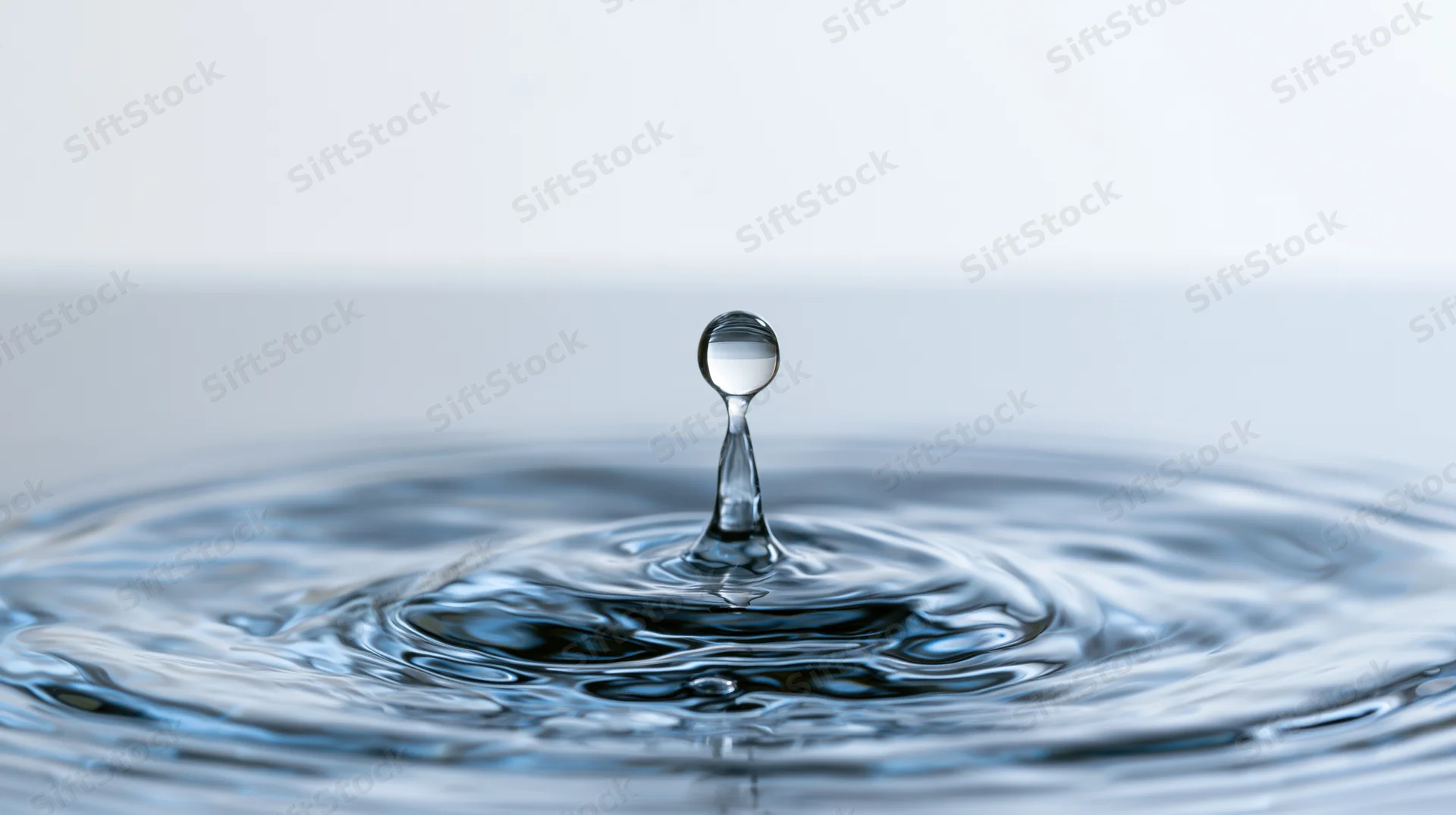 Water droplet suspended above rippling surface in calm liquid