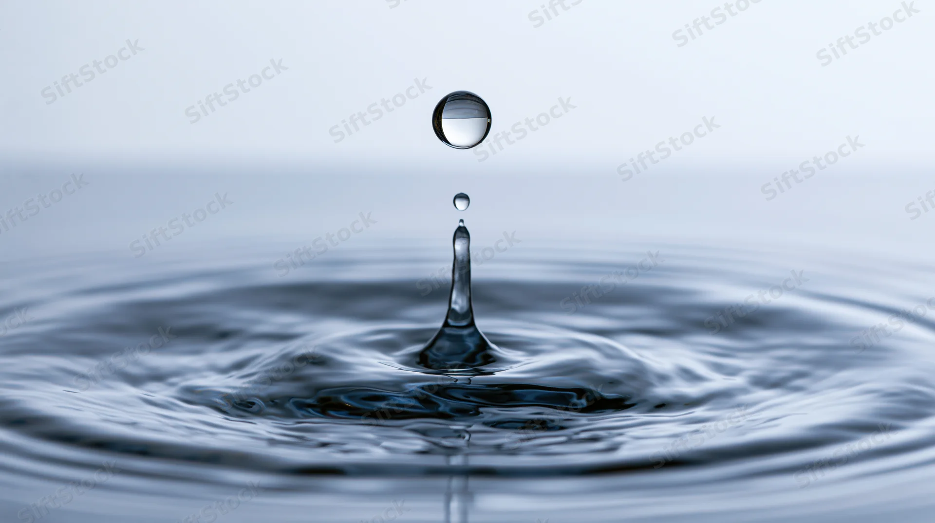 Water droplet suspended above rippling surface in closeup view
