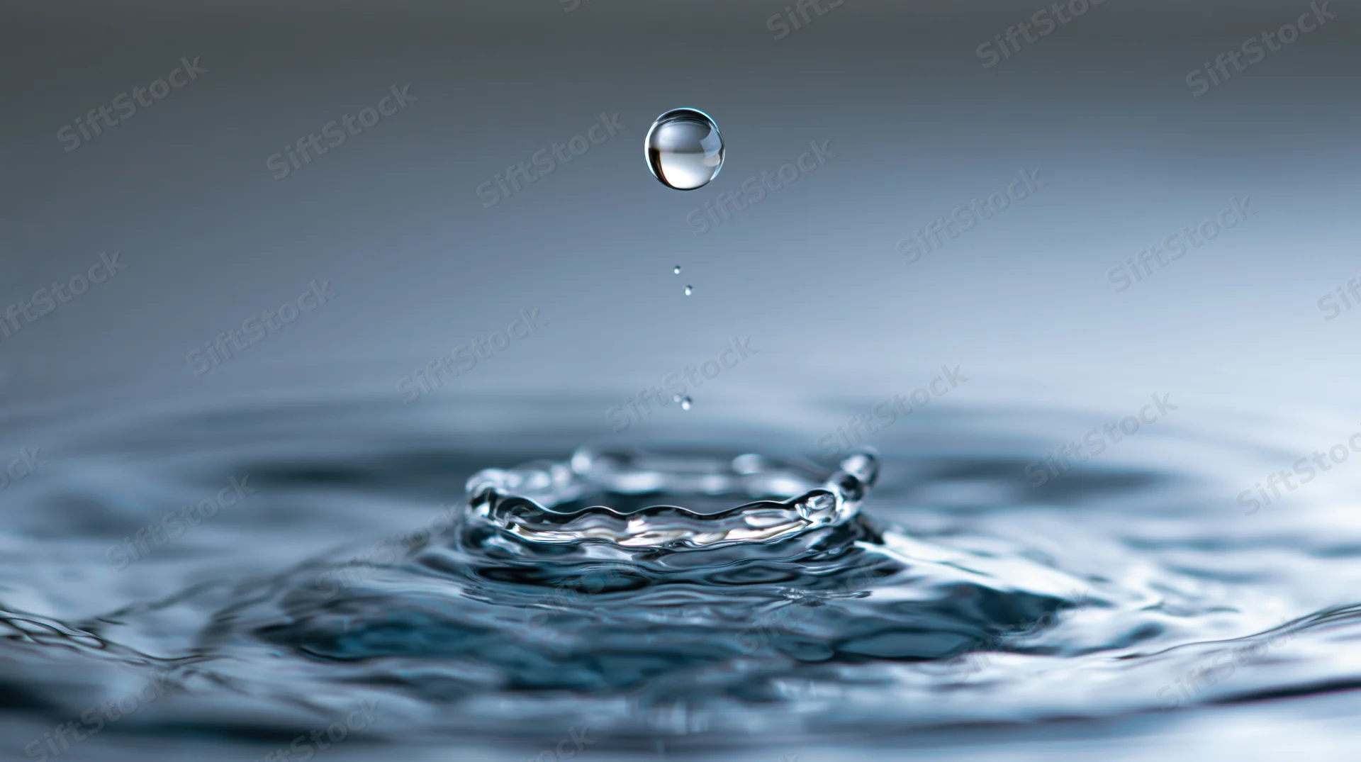 Water droplet suspended above a crown splash on a calm surface