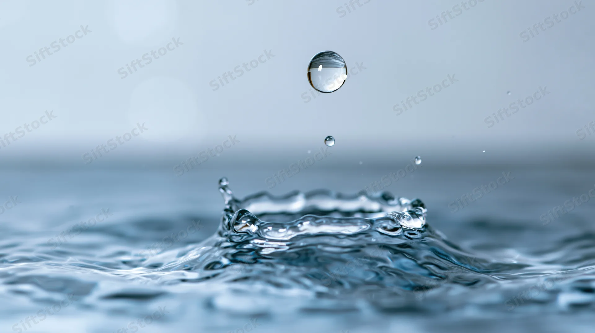 Water droplet suspended above a crown splash on a calm surface