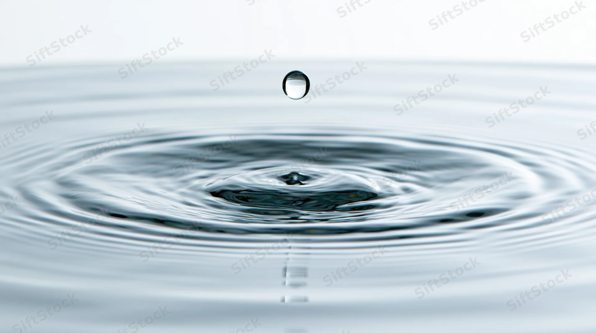 Single water droplet suspended above rippling surface in calm still water
