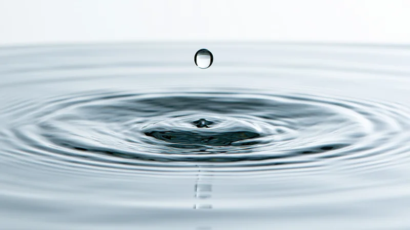Single water droplet suspended above rippling surface in calm still water